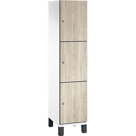 Hoher Schrank mit Holzoptikfronten. Die Türen sind dreifach unterteilt und mit silbernen Knäufen versehen. Der Schrank steht auf schwarzen Füßen.