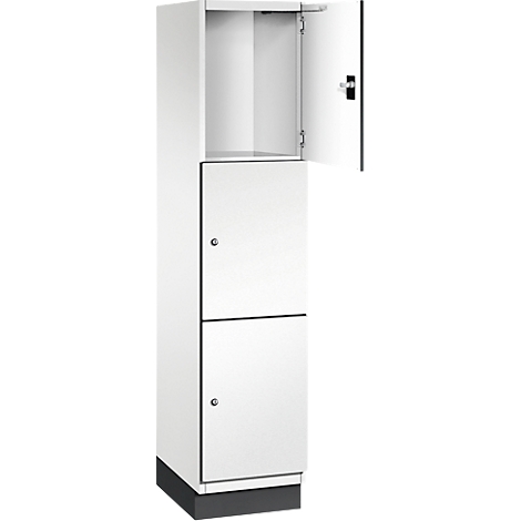 Ein weißer Spind, die obere Tür ist geöffnet. Der Spind steht auf einem dunklen Sockel.