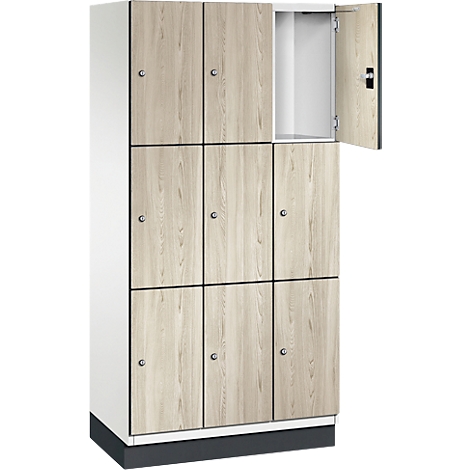 Mehrteiliger Spind, eine Tür geöffnet. Helle Holzoptik, dunkle Türrahmen und Sockel, ein weißer Korpus.