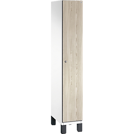 Ein weißer Schrank, mit einer Tür in Holzoptik, steht auf schwarzen Füßen.