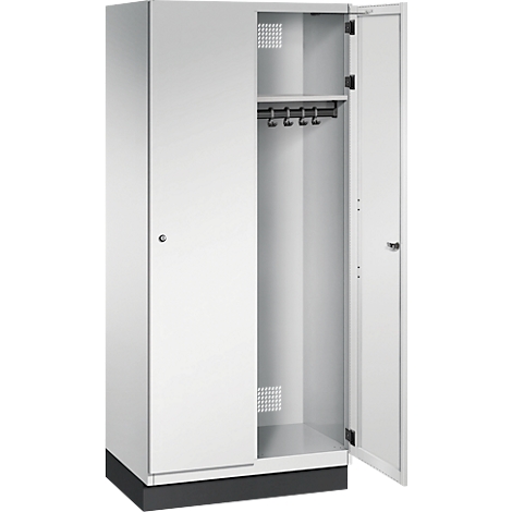 Weißer Spind mit zwei Türen, eine ist offen. Im Inneren sind Kleiderhaken und ein Regal zu sehen.