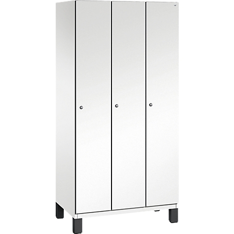 Weißer Kleiderschrank mit drei Türen, schmalen schwarzen Griffen und schwarzen Füßen.