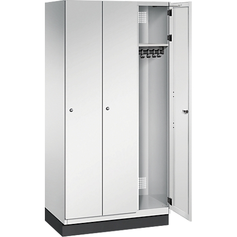 Weißer Stahlschrank mit drei Türen, eine Tür geöffnet. Im Inneren: Haken für Kleidung und ein Regal.