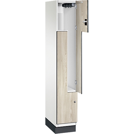 Een open kast met een witte behuizing en houten deuren. De bovenste deur staat open, met een kleerhanger. De kast staat op een voet.