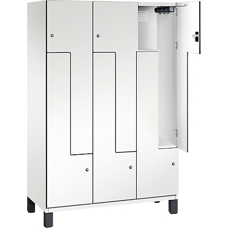 Weißer Spind mit mehreren Fächern, eine Tür geöffnet. Schwarze Umrandung, schwarze Füße.