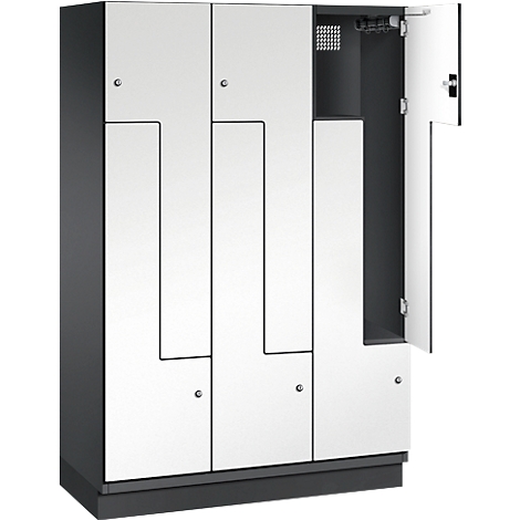 Grauer Spind mit weißen Türen. Eine Tür ist geöffnet, dahinter ist ein Stauraum mit Lüftungsgittern und Haken erkennbar.