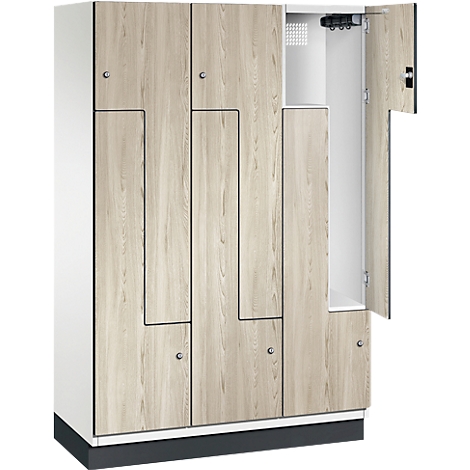 Ein Schrank mit Holzlaminat-Optik. Eine Tür ist geöffnet, dahinter Regale und Haken. Der Schrank steht auf einem schwarzen Sockel.