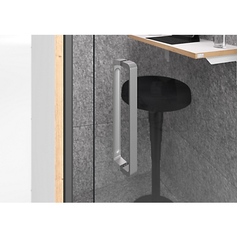 Gros plan : poignée de porte argentée sur la porte vitrée d'une cabine téléphonique de bureau. A côté, un tabouret noir et une table blanche.