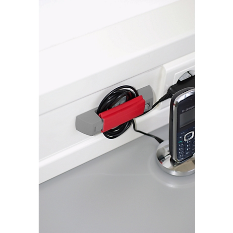 A grey cable holder with a red holder, to which a black cable is attached. Next to it a mobile phone in a charging cradle.