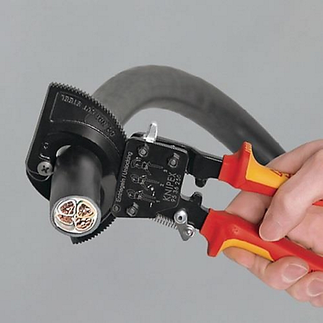 Person cutting a cable with pliers. The pliers are black and red, the cable black. The cable cross-section is visible.