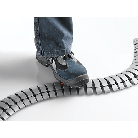 A foot in jeans and safety shoe stands on a gray cable duct.