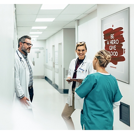 Trois professionnels de santé discutent dans un couloir d'hôpital lumineux à côté d'une affiche de don de sang.