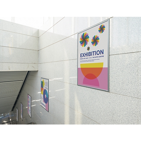 Plusieurs affiches d'exposition sont accrochées sur un mur clair carrelé le long d'un escalier.