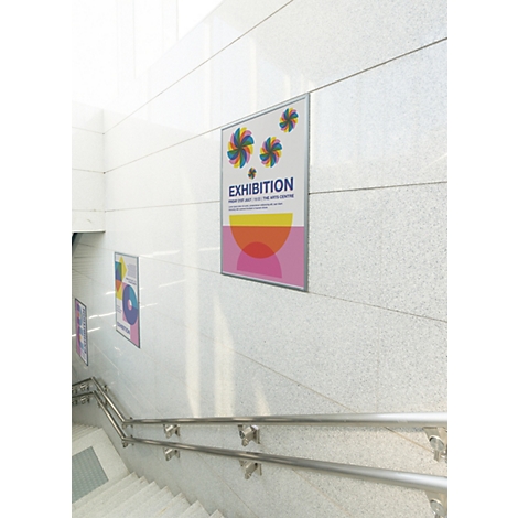 Affiche d'exposition avec des cercles colorés sur un mur d'escalier en marbre clair.