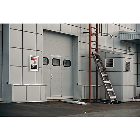 Bâtiment industriel avec une porte sectionnelle grise et une échelle en métal rouge contre la façade grise.