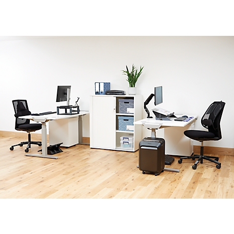 Bureau avec deux espaces de travail : bureaux réglables en hauteur, chaises de bureau, déchiqueteuse et armoire. Plancher en bois.