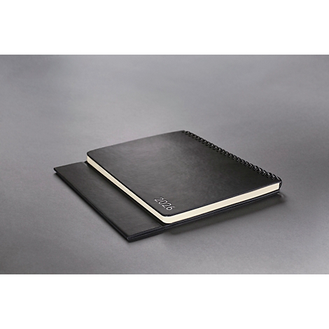 Cahier noir avec l'empreinte '2026'. Il repose sur un autre cahier sur fond gris.