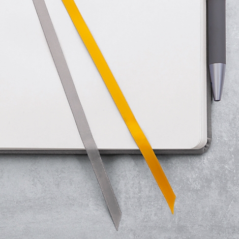 Carnet avec deux signets, un gris et un jaune. Un stylo est posé sur le bord.