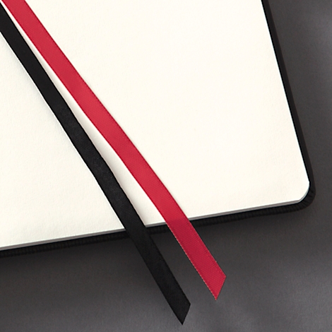 Gros plan d'un carnet avec des signets en ruban rouge et noir dépassant du coin.