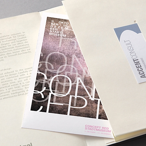 Une brochure triangulaire avec le mot "CONCEPT" et des textes en allemand. A côté, une carte de visite avec "ACCENTCONSULT".
