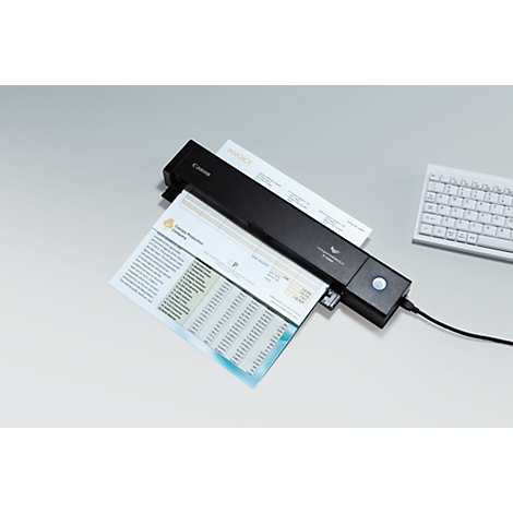 A black Canon scanner scanning documents. Part of the keyboard is visible in the background.
