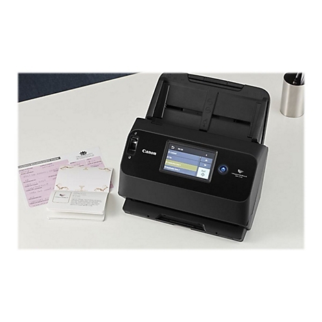 Ein schwarzer Canon-Scanner steht auf einem weißen Tisch neben Dokumenten und einem Becher. Auf dem Bildschirm werden Menüpunkte angezeigt.