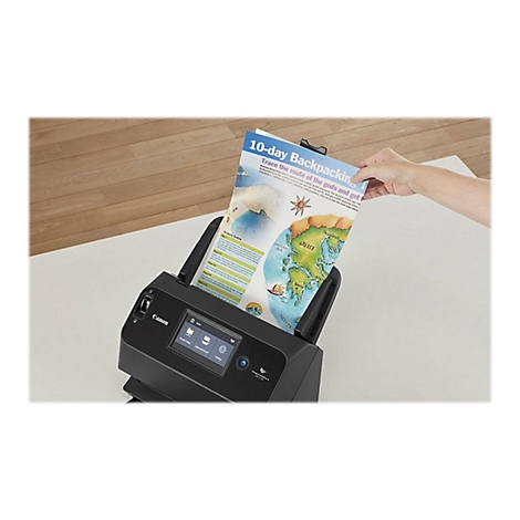 Eine Hand hält ein Blatt Papier in einen schwarzen Canon-Scanner. Auf dem Blatt stehen "10-Tages-Backpacking" und eine Weltkarte.
