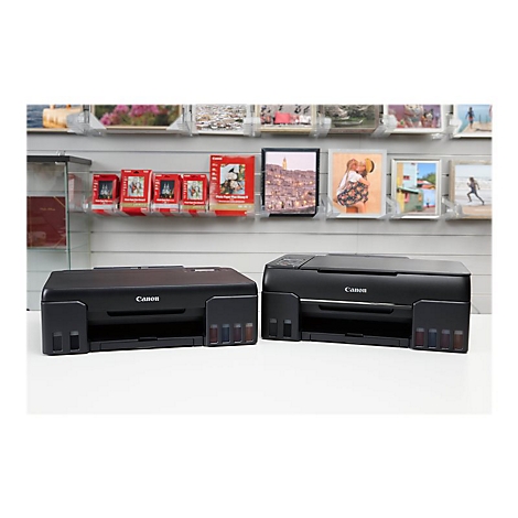 Zwei schwarze Canon-Drucker stehen nebeneinander. Im Hintergrund sind Fotos und Bilder ausgestellt.