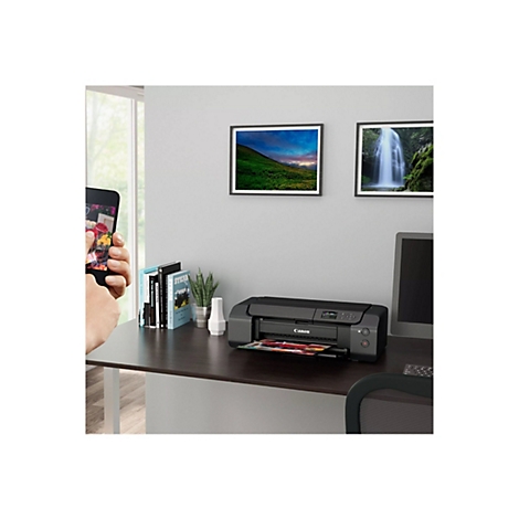 Ein Drucker steht auf einem Schreibtisch. Auf dem Display werden Bilder angezeigt, daneben liegt ein Smartphone mit einem Blumenstrauß-Foto.