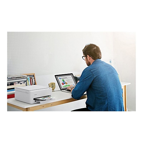 Ein Mann sitzt an einem Schreibtisch und arbeitet mit einem Laptop und einem Drucker. Der Drucker druckt Papier aus.