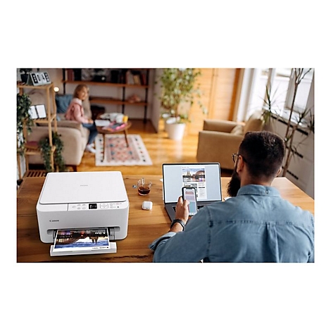 Mann druckt mit Canon-Drucker in hellem Wohnzimmer, im Hintergrund sitzt ein Kind.