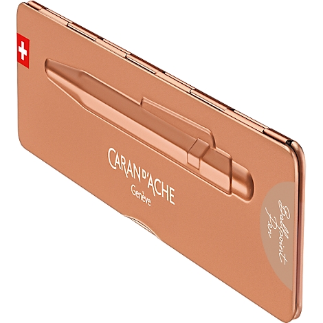 Eine kupferfarbene Stiftverpackung mit einem Schweizer Kreuz, dem Schriftzug CARAN D'ACHE Genf und dem Hinweis „Ballpoint Pen”.