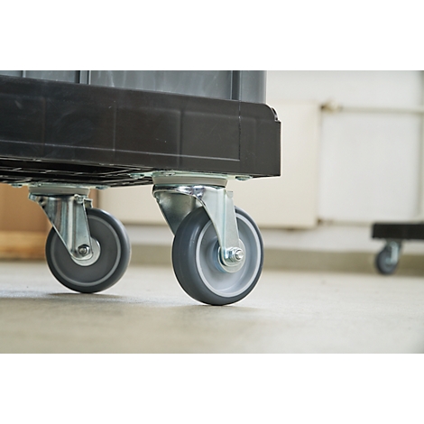 Primer plano de dos ruedas grises debajo de un contenedor de plástico negro. De pie sobre un suelo claro.