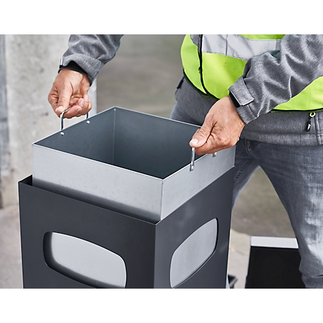 Personne tenant un conteneur métallique amovible au-dessus d'un conteneur à déchets gris.