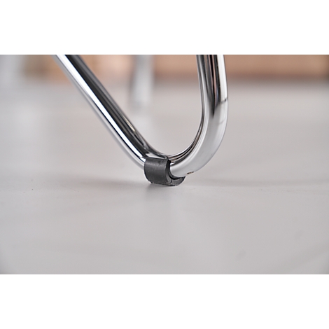 Gros plan d'un pied de chaise chromé reposant sur une surface claire. Une bague en caoutchouc noir est attachée en guise de protection.