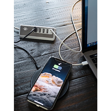 Smartphone se charge sans fil sur un socle de chargement, à côté d'un ordinateur portable et d'un hub USB sur une surface en bois. La batterie affiche 82% de charge.