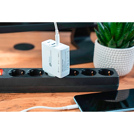 Chargeur blanc branché sur une multiprise noire, câbles connectés à un smartphone. Plante en arrière-plan.