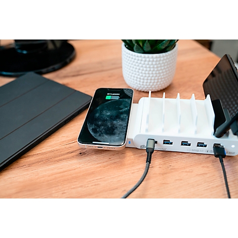 Un smartphone en charge sur une station de charge blanche avec plusieurs ports. Une tablette noire se trouve à côté.