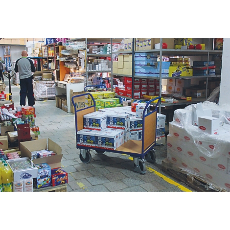 Homme dans un entrepôt, chariot chargé de boîtes. Étagères avec des marchandises en arrière-plan.
