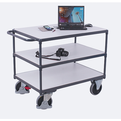Un chariot de service à trois niveaux avec ordinateur portable, appareil photo et accessoires. Cadre gris, étagères blanches, roues.