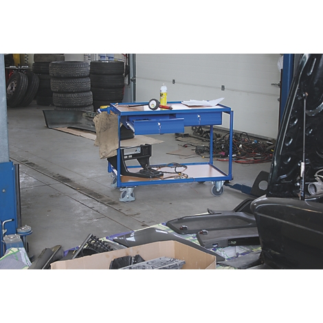 Boîte à outils bleue sur roues. Pile de pneus, outils et une voiture en arrière-plan.