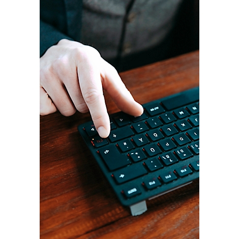 Gros plan d'une main appuyant sur une touche d'un clavier noir. Le fond est flou et montre une table en bois.