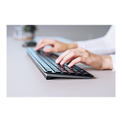 Nahaufnahme einer Person, die auf einer schwarzen Tastatur tippt. Helle Umgebung, weiße Manschette sichtbar.