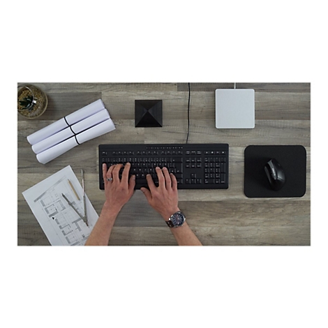 Person tippt auf schwarzer Tastatur. Daneben liegen ein Mauspad, eine Maus, PlÃ¤ne und ein weiÃŸes KÃ¤stchen.