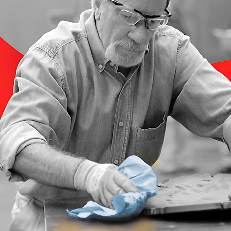 Un homme avec des lunettes et une barbe essuie une surface avec un chiffon bleu. Il porte des gants.