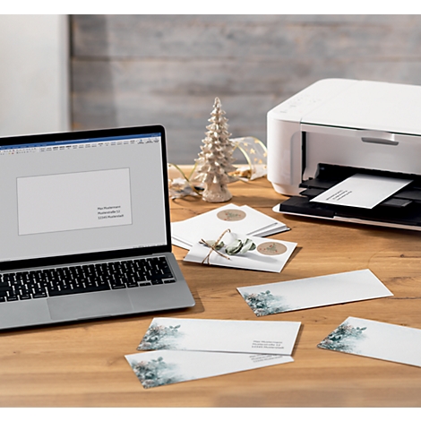 A laptop and a printer on a wooden table, with Christmas cards. The printer is printing a card.