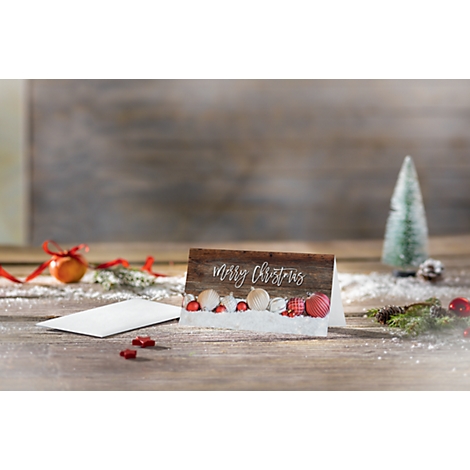Christmas card with 'Merry Christmas' lettering on wood look. In front of it, small decorative objects in a winter landscape.