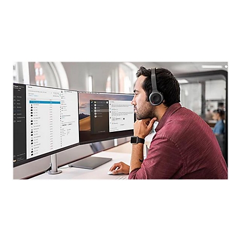 Ein Mann mit Headset sitzt vor zwei Monitoren. Er betrachtet den rechten Bildschirm. Am Handgelenk trÃ¤gt er eine Smartwatch.