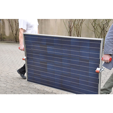 Two people carry a large solar panel made of dark blue material.