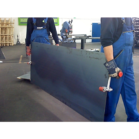 Two workers carrying a large steel plate in a factory. One has a white gripper with a red handle in his hand.